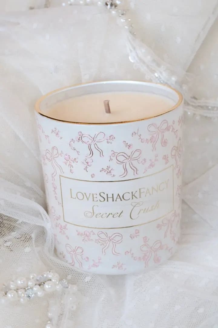 Close-up of the unlit Secret Crush candle with cream wax and gold rim, nestled in white tulle with pearl trim