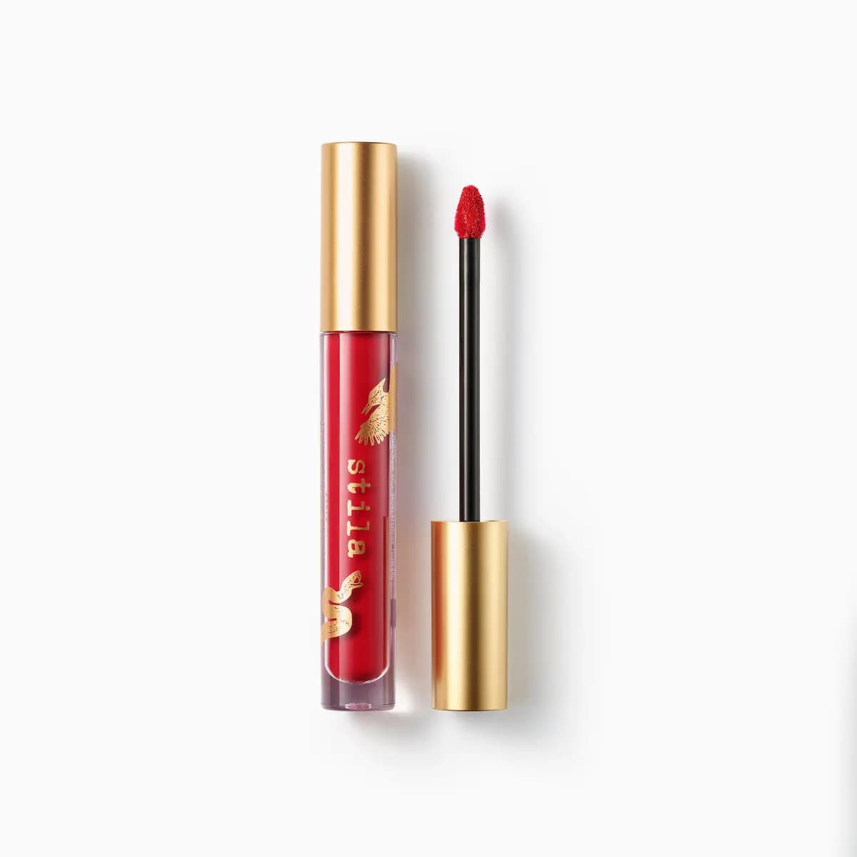 Red liquid lip in a clear tube with gold bird and snake print, beside its gold cap and doe-foot applicator