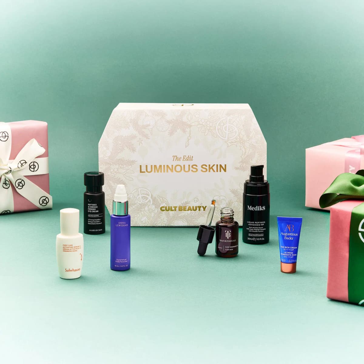 Luminous Skin box with Medik8, Sulwhasoo, Emma Lewisham and Augustinus Bader skincare on teal beside wrapped gifts