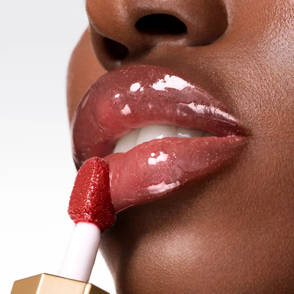 Close-up of glossy, sparkly berry-red lip oil being applied to full lips with a red doe-foot applicator