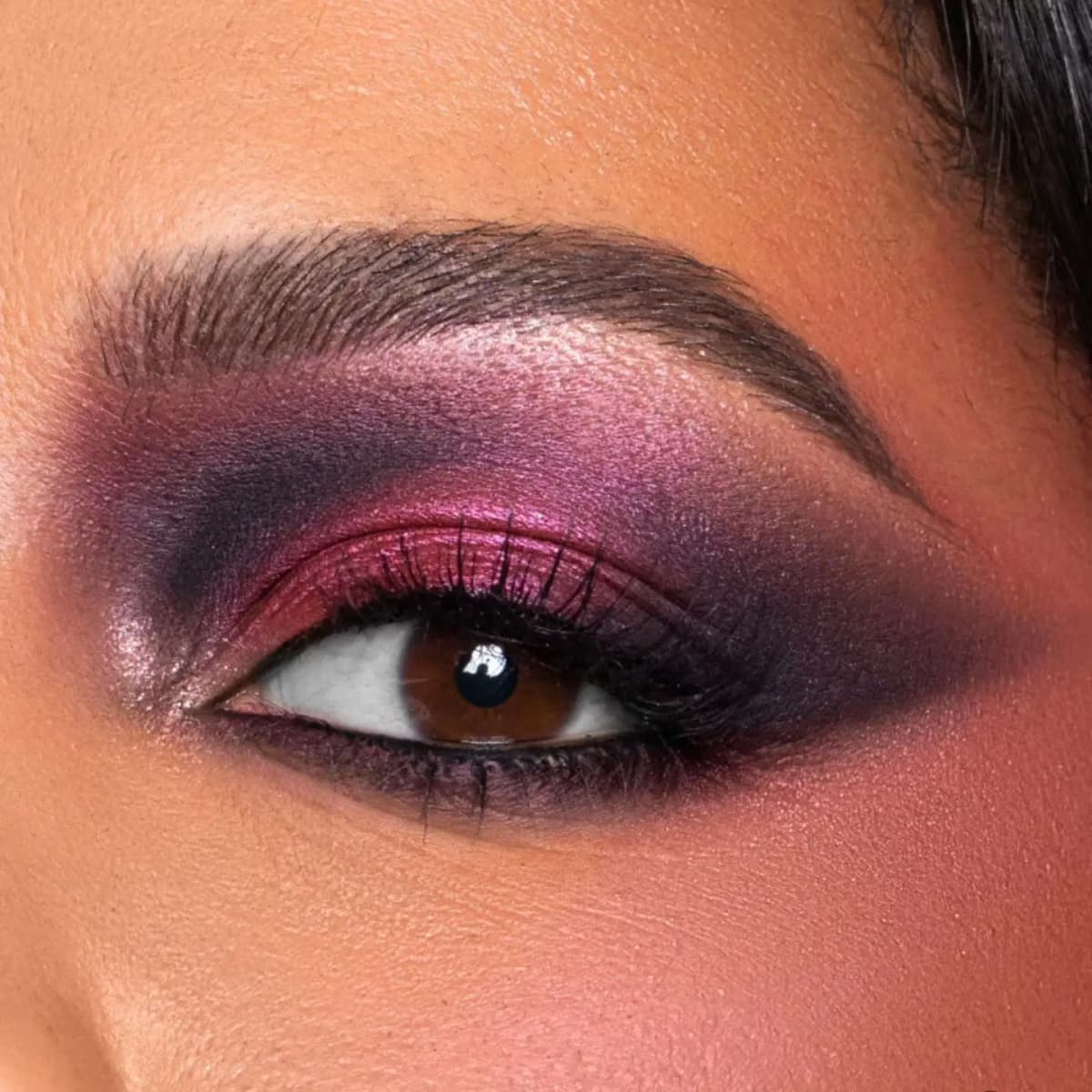 Close-up eye with shimmery magenta lid and blown-out smoky plum crease on medium-deep skin