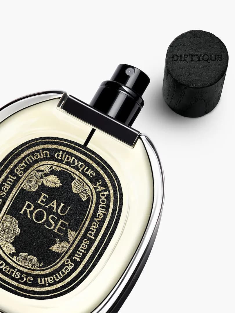 Close-up of uncapped Eau Rose bottle with gold roses on its black label and wooden cap