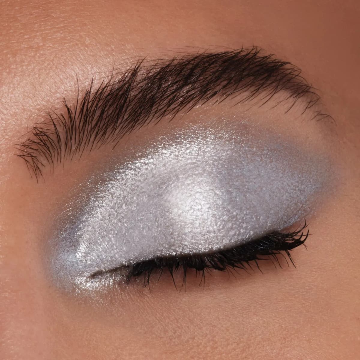 Closed eye with an icy silver metallic shadow covering the lid, paired with black lashes and a bold brow