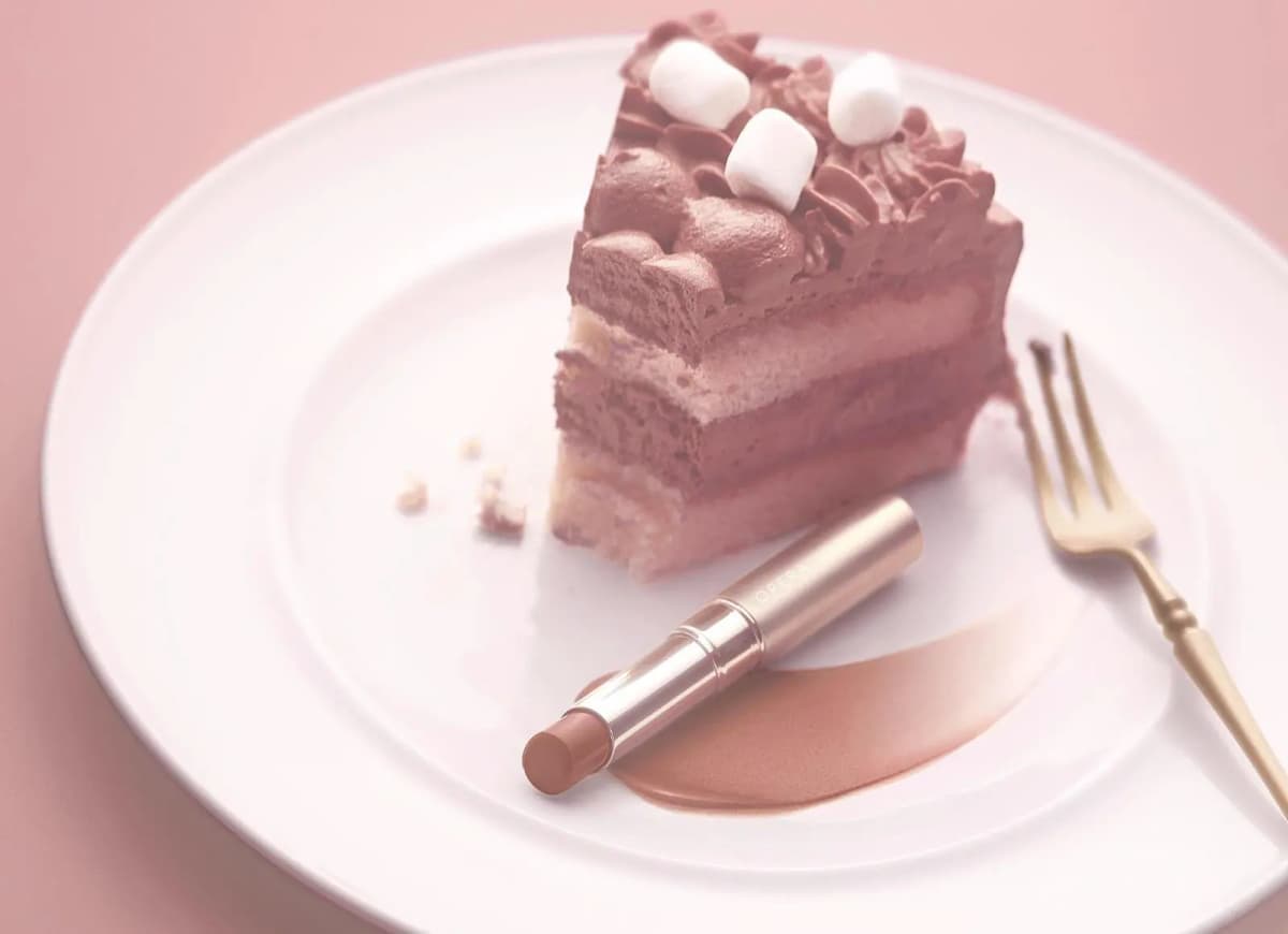 OPERA lipstick in Cinnamon Brown on a plate with a smear of colour, beside a chocolate layer cake with marshmallows