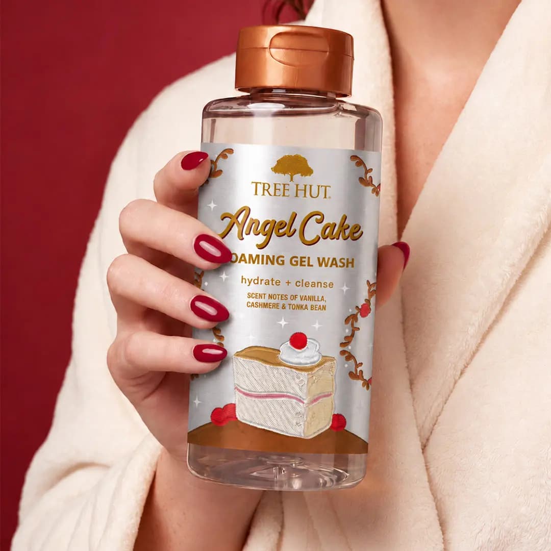Hand with red nails holding the Foaming Gel Wash bottle against a cream robe and deep red background