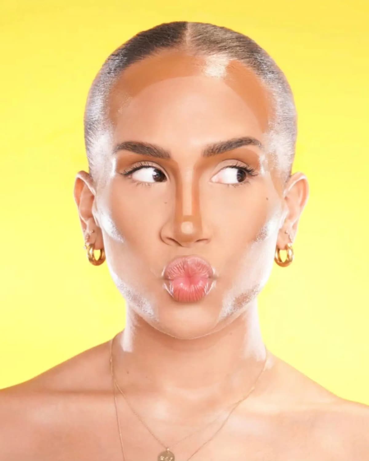 Model on a yellow backdrop with unblended cream contour and highlight, puckering lips and glancing sideways