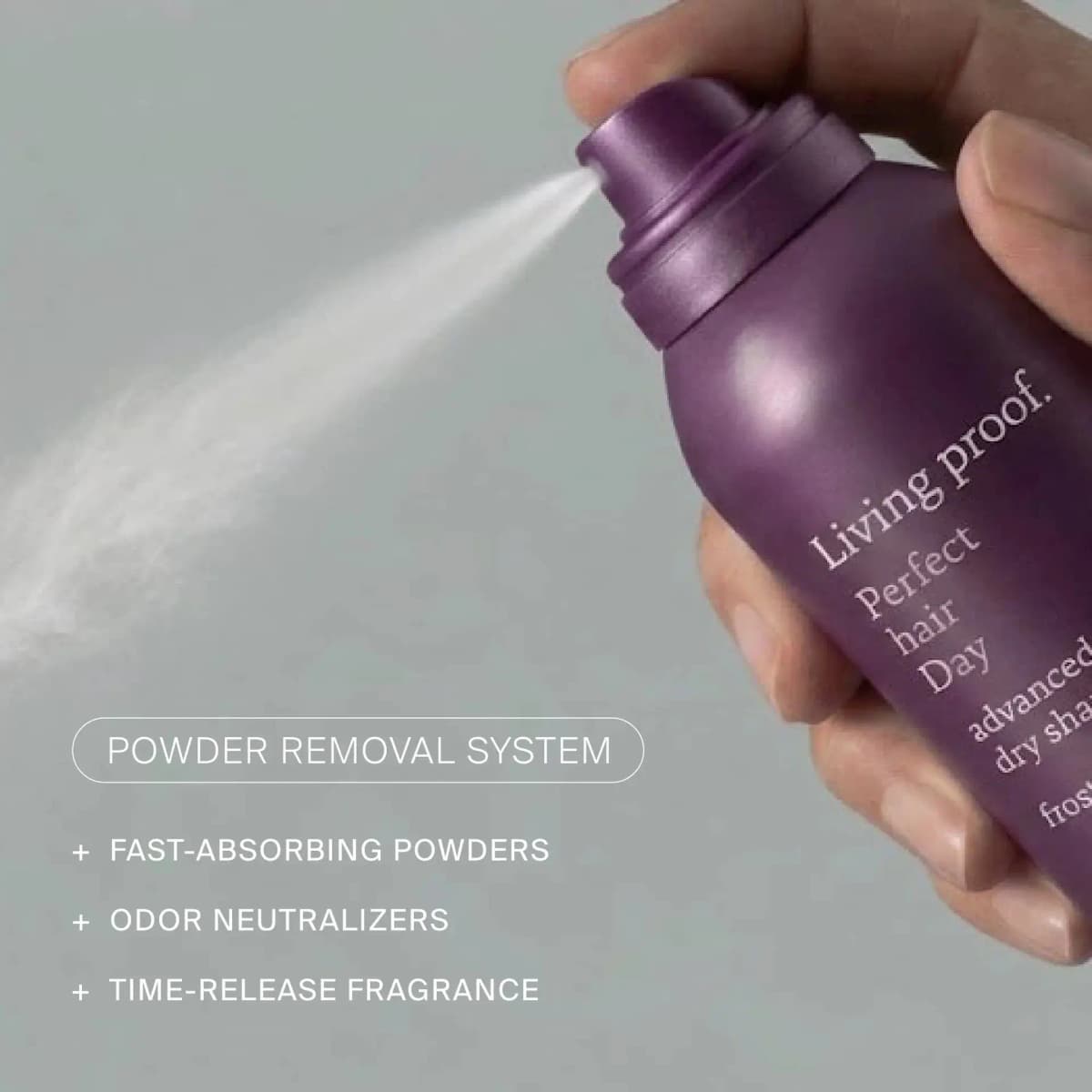 Hand spraying a fine white mist from a purple Perfect Hair Day can, with Powder Removal System feature list