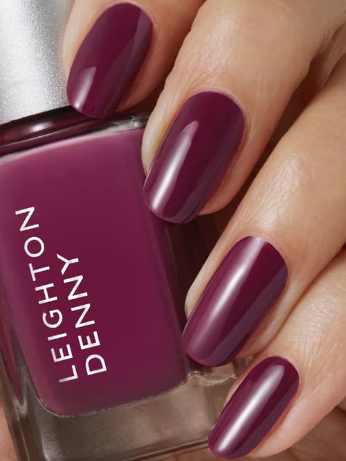 Glossy deep plum manicure on oval nails held beside a Leighton Denny Tough Love bottle