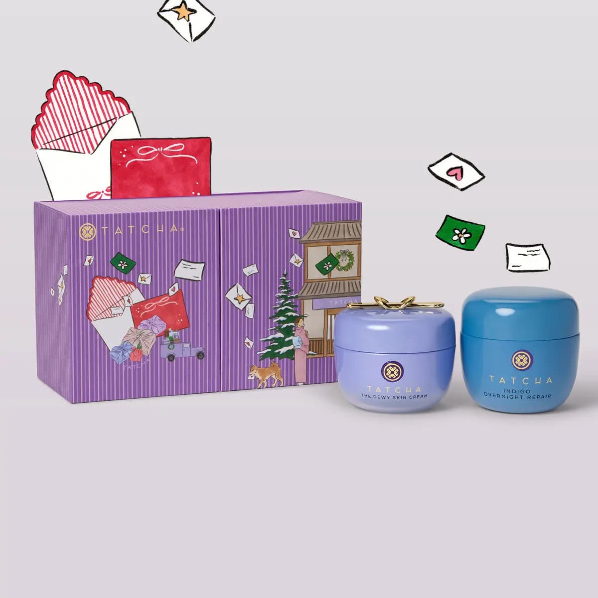 Wide purple Tatcha box with The Dewy Skin Cream and Indigo Overnight Repair jars, illustrated envelopes floating above