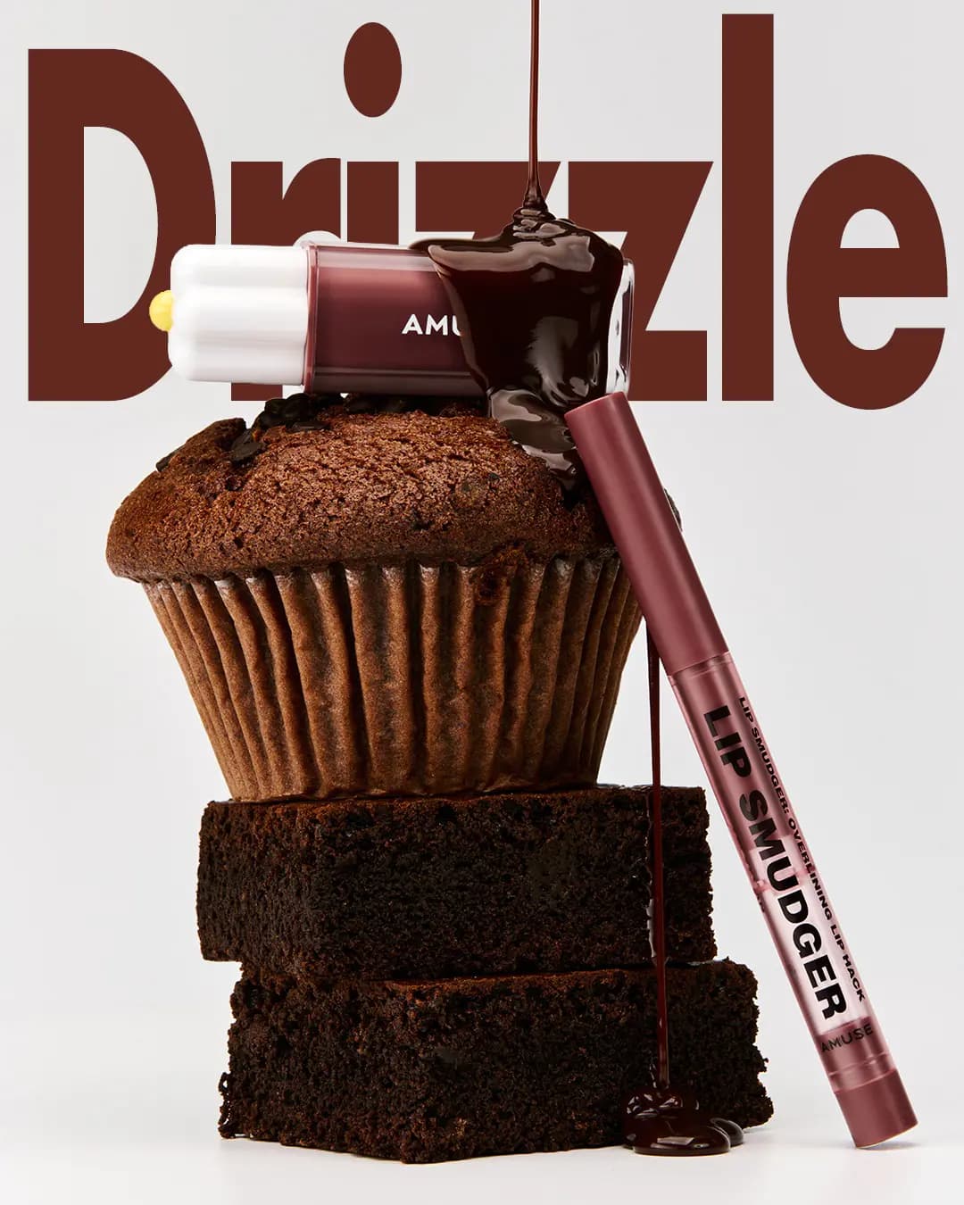 Chocolate syrup drips onto an AMUSE lip tint bottle atop a chocolate muffin and brownies, with 'Drizzle' text behind