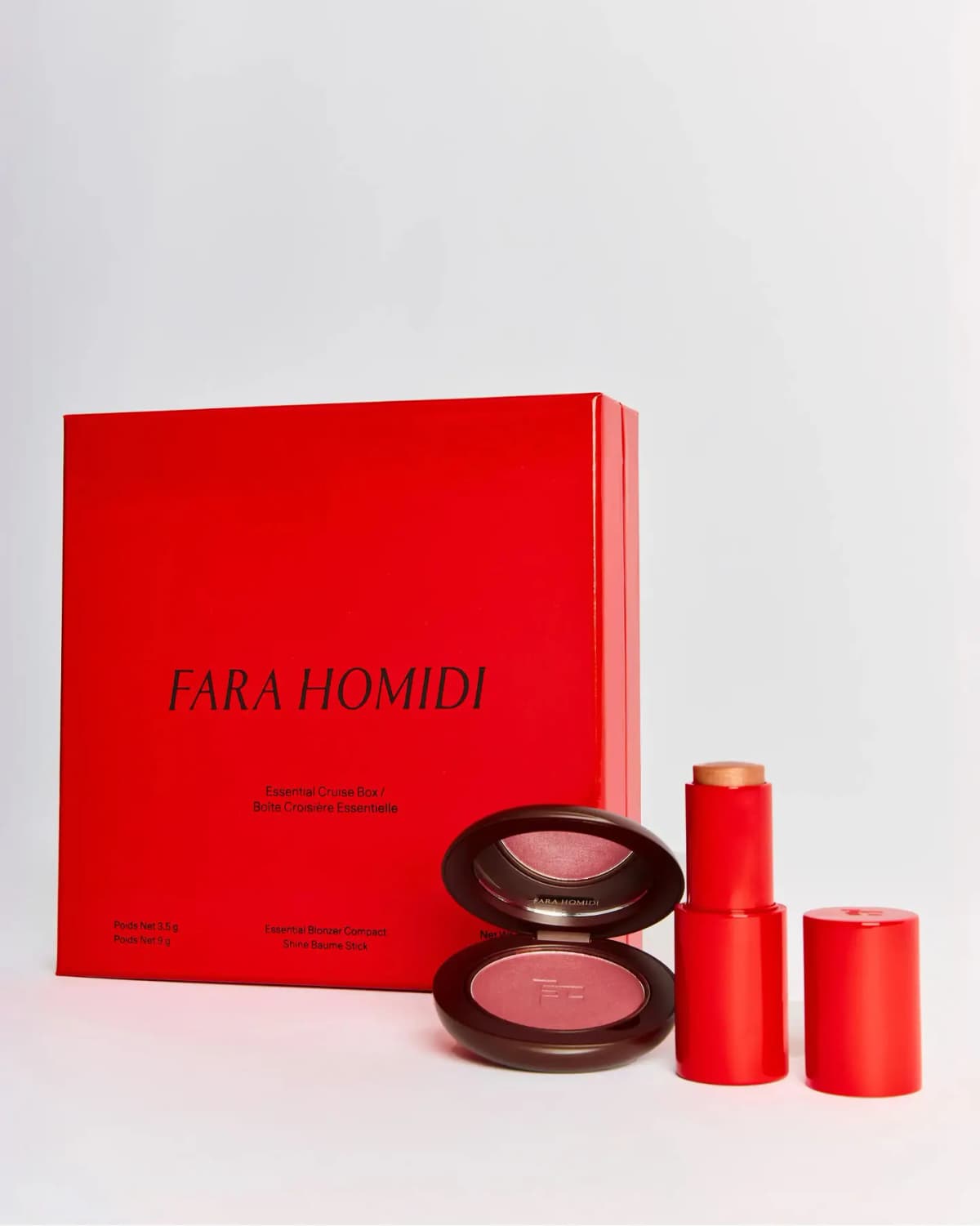Red Essential Cruise Box standing behind an open brown compact of pink blush and an uncapped red Shine Baume Stick