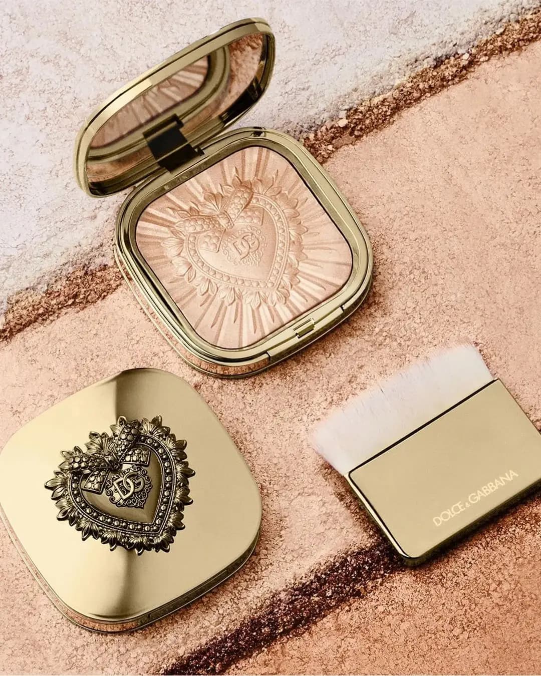 Open mirrored compact, closed heart-topped lid and Dolce&Gabbana flat brush on swatched powder stripes