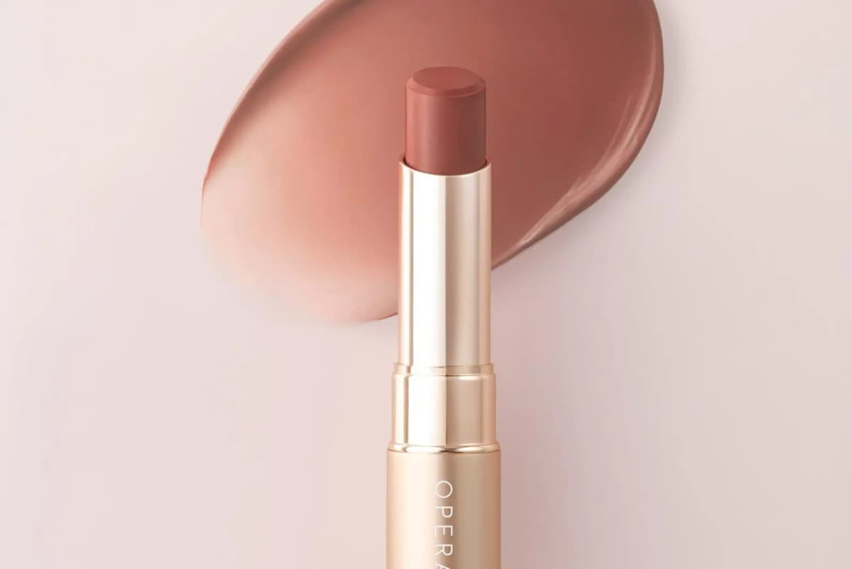 OPERA Sheer Matte Lipstick in Cinnamon Brown, rose-gold tube open against a creamy warm brown swatch on a pale pink