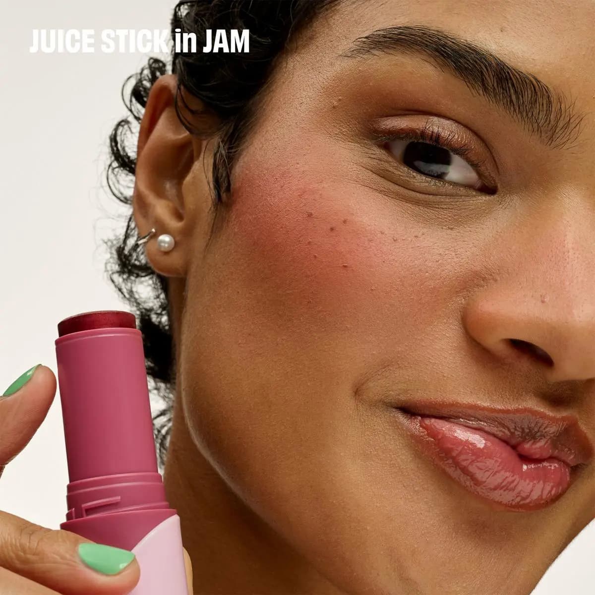 Model with berry-flushed cheek and glossy lips holds a pink Juice Stick in Jam to her face