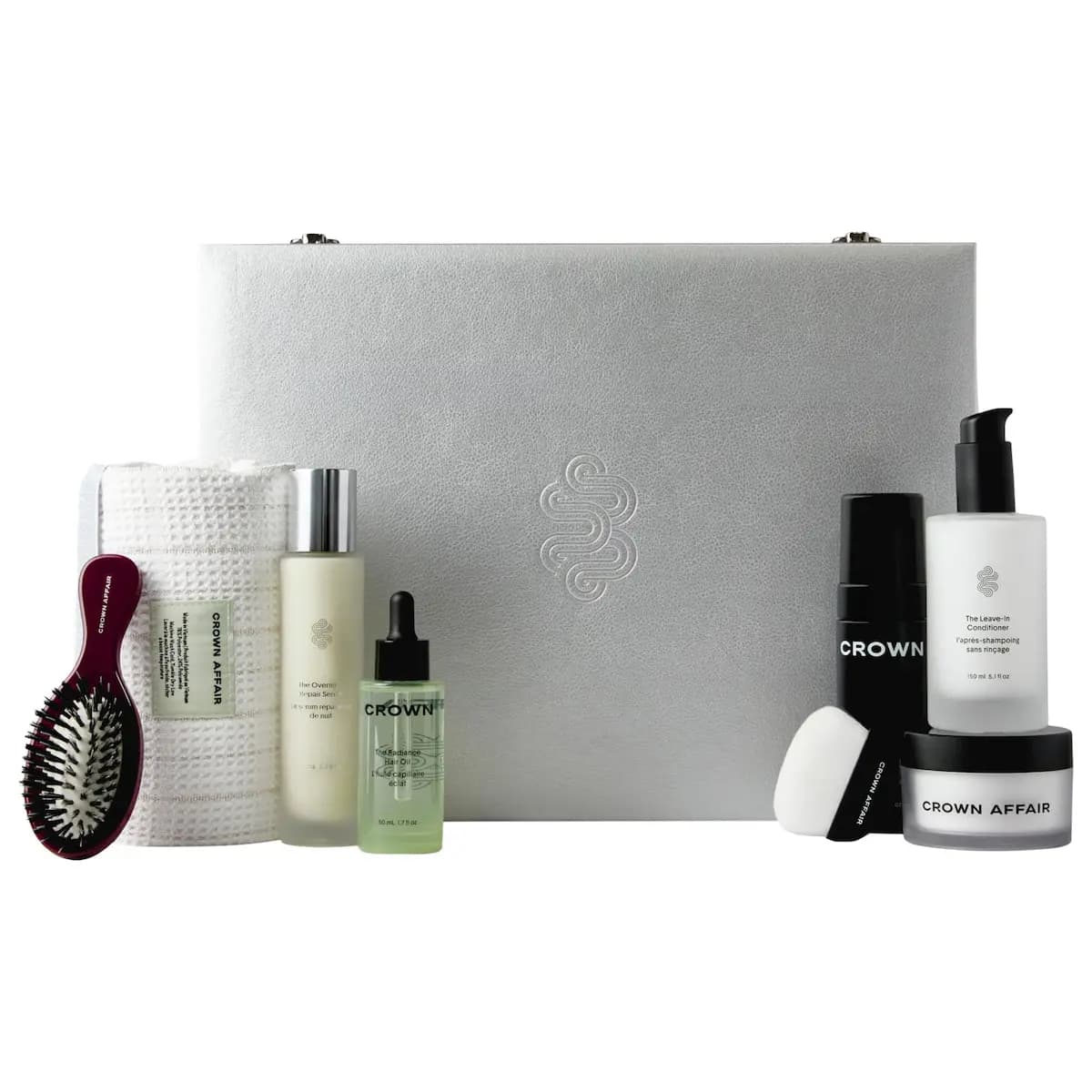 Silver textured Crown Affair Vault case flanked by brush, towel, serum, Radiance Hair Oil, mousse, leave-in and jar