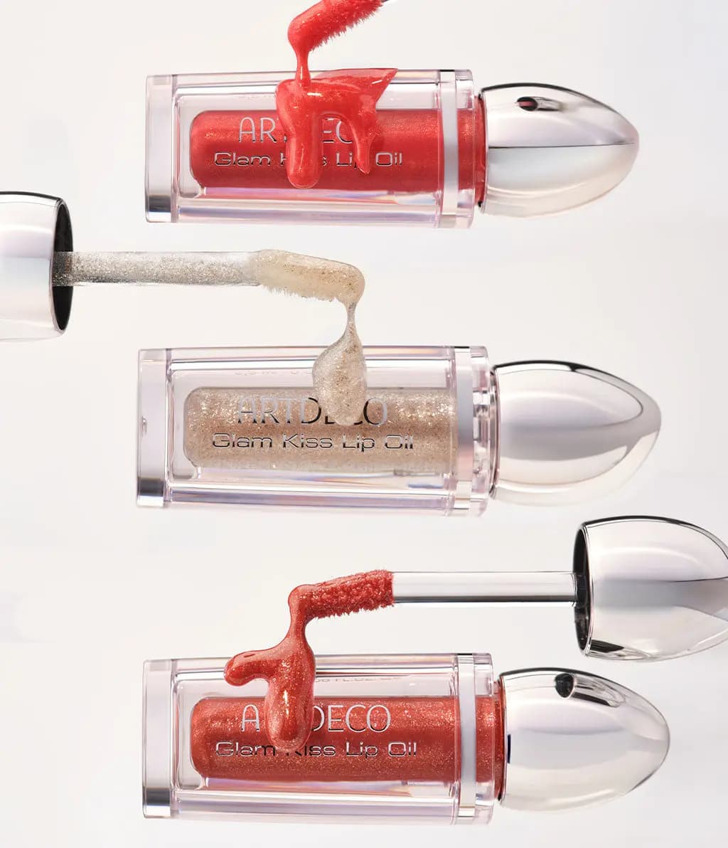 Three Glam Kiss Lip Oils lying sideways, red, gold glitter and copper, with glossy oil dripping from applicators