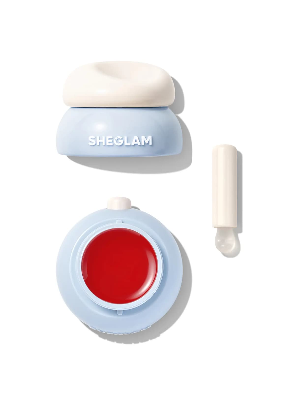 Blue jar with cream lid, open pan of bright red jelly lip mask and white silicone-tipped applicator on white