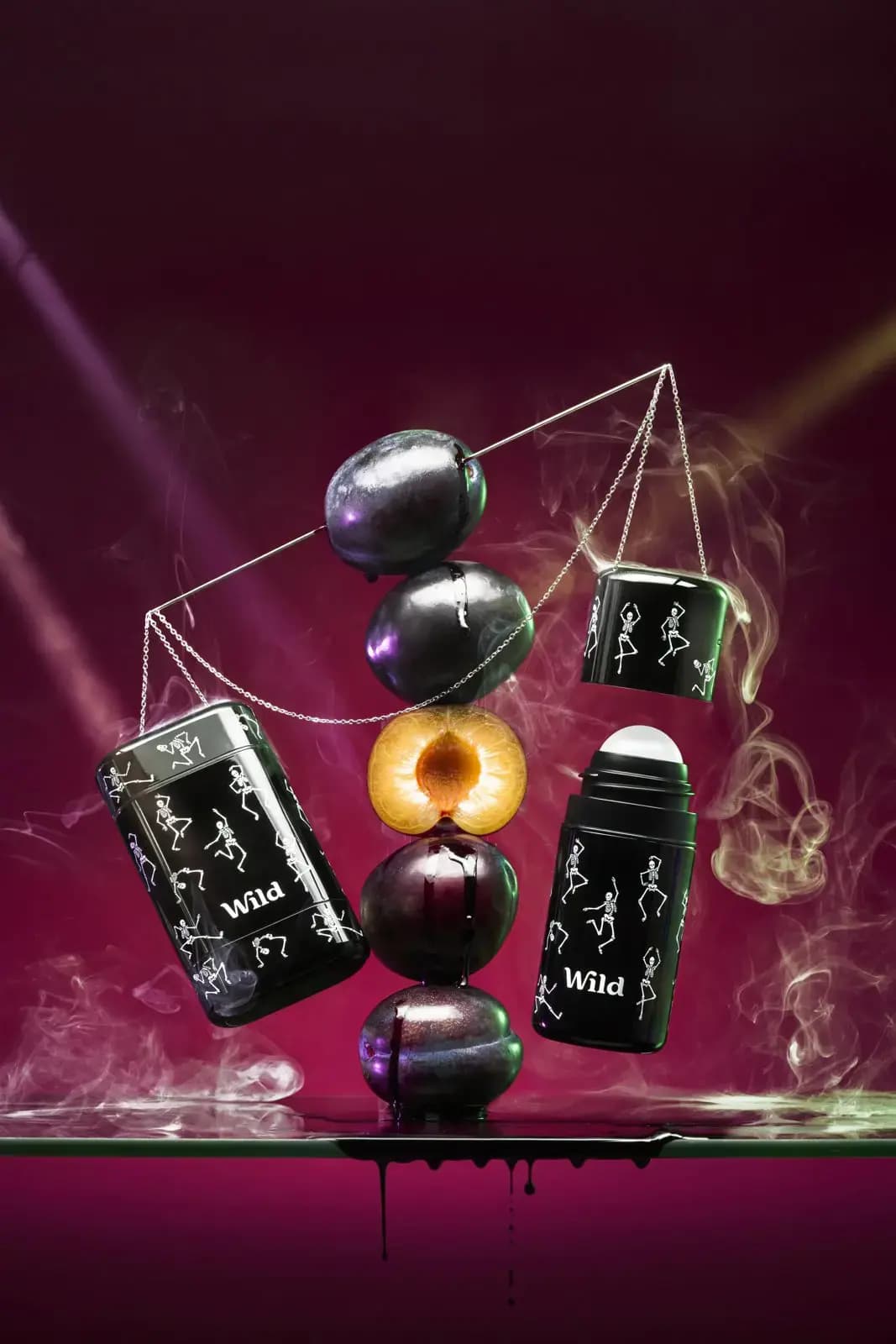 Wild Dancing Skeletons stick case and roll-on hang from chains beside a stack of plums, one halved