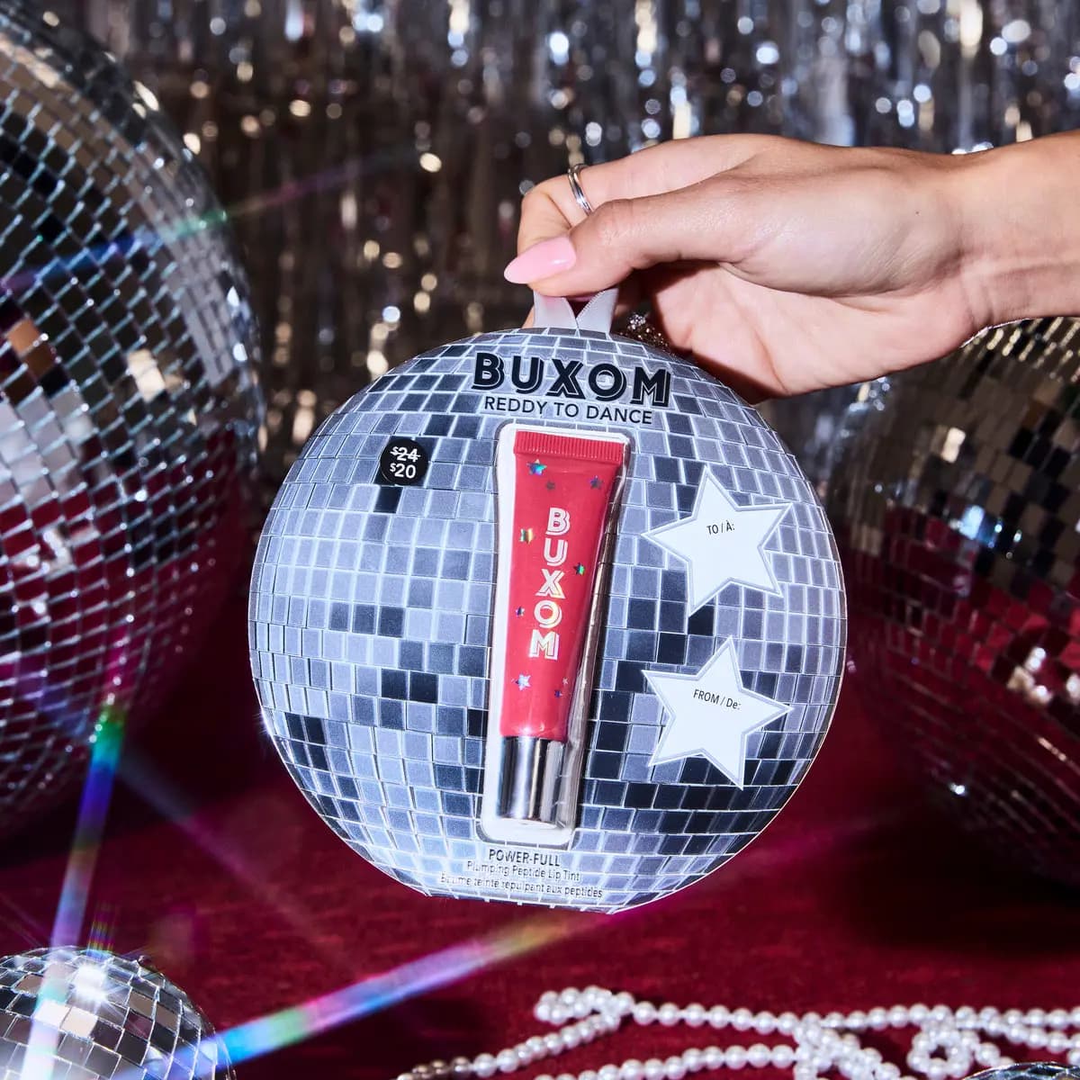 Hand holding the silver disco-ball ornament pack containing Reddy to Dance against a sparkly party backdrop