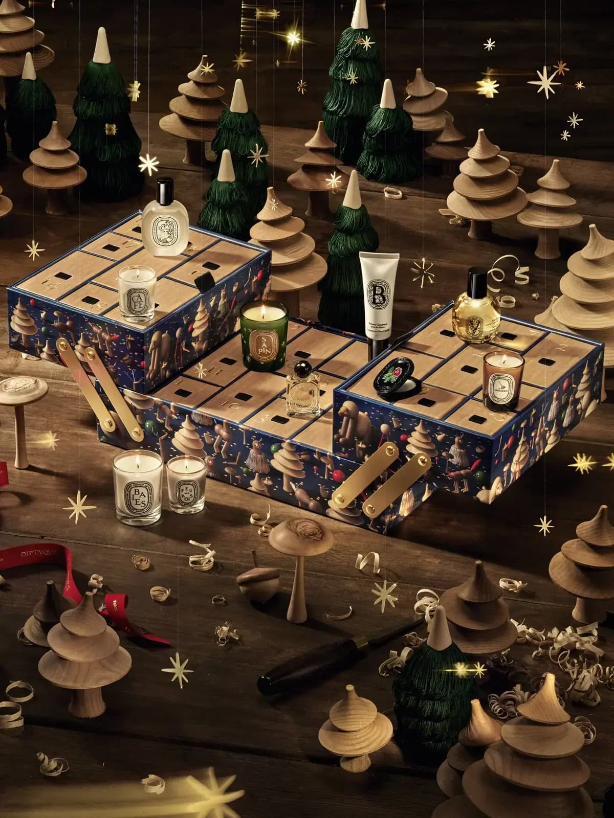 Diptyque advent calendar in a blue illustrated box with candles, fragrances and hand balm among wooden trees