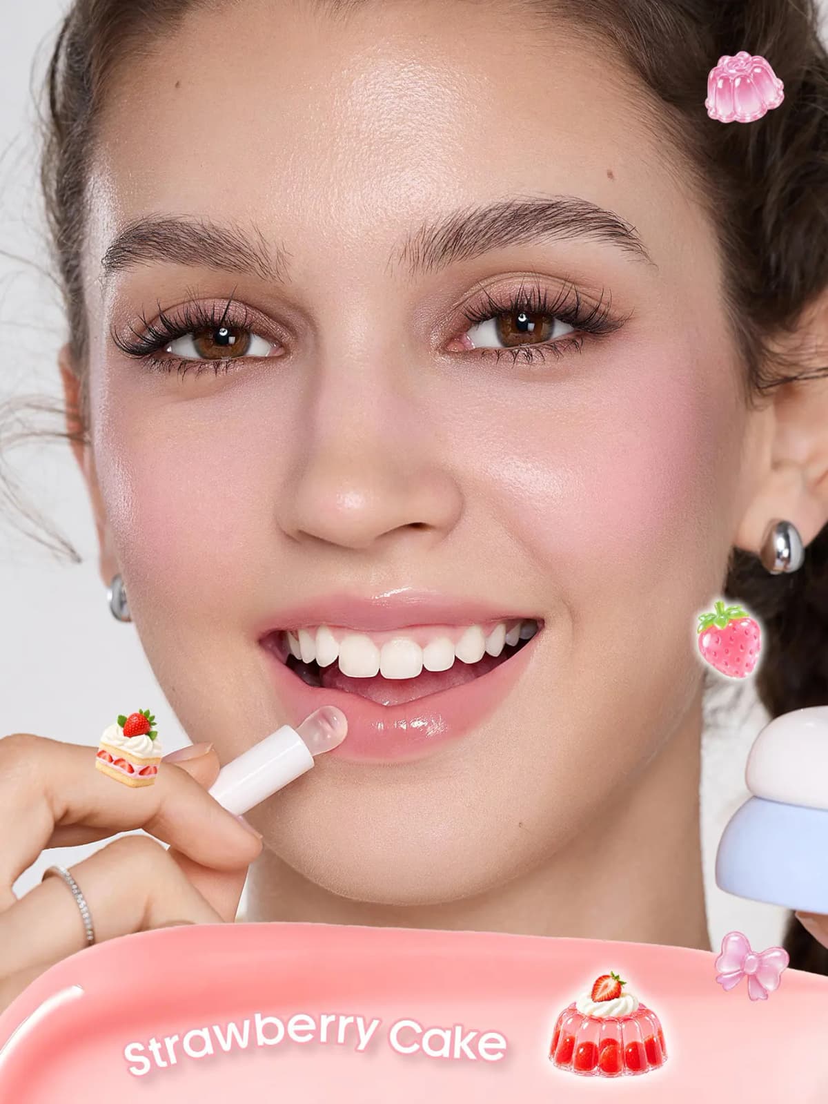 Smiling model applying sheer pink gloss with a white applicator, holding a blue jar, labelled Strawberry Cake