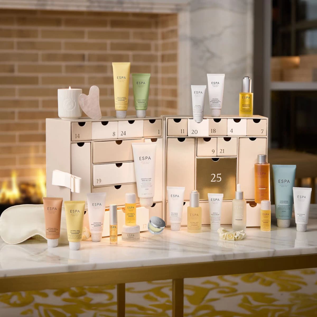 ESPA Moments of Wellness Advent Calendar opened with numbered drawers, products, candle and gua sha on marble by a fireplace