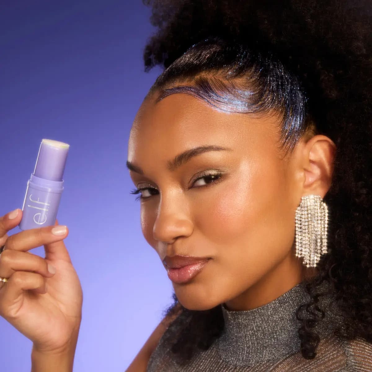 Model with voluminous curls and glittering edges holds up the lilac hair stick near her face.