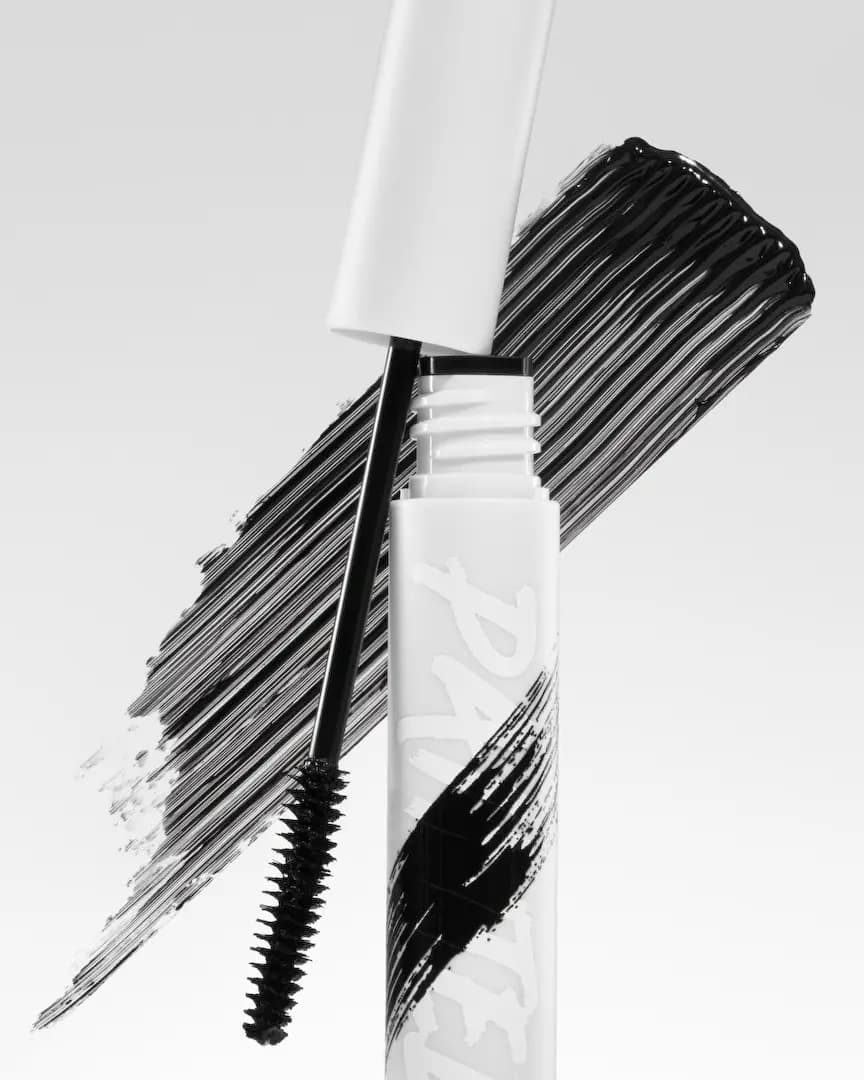 Open white tube with black spoolie wand against a glossy black mascara swatch