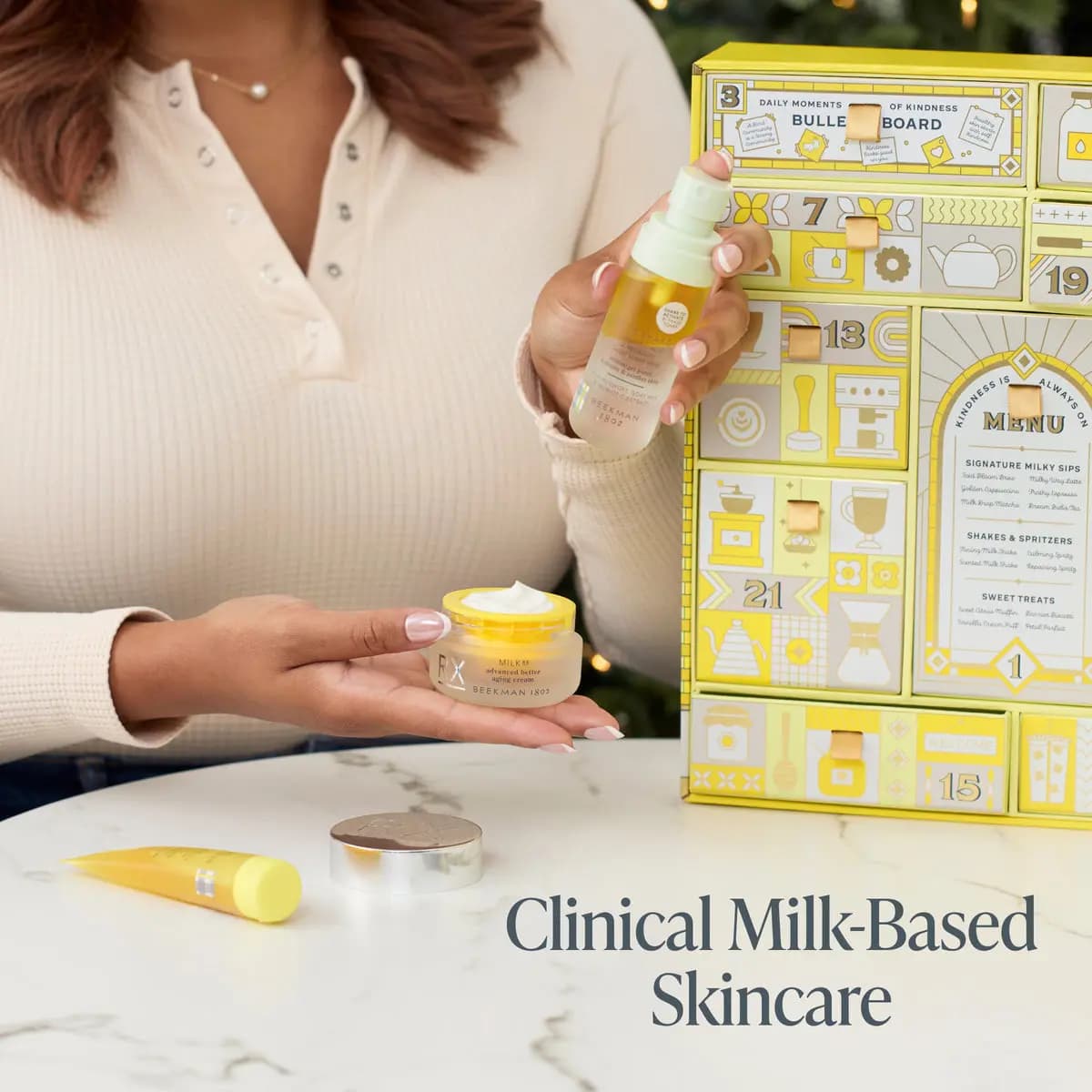 A hand holds Milk Shake toner mist and a jar of MilkRX advanced better aging cream beside the open yellow calendar drawers
