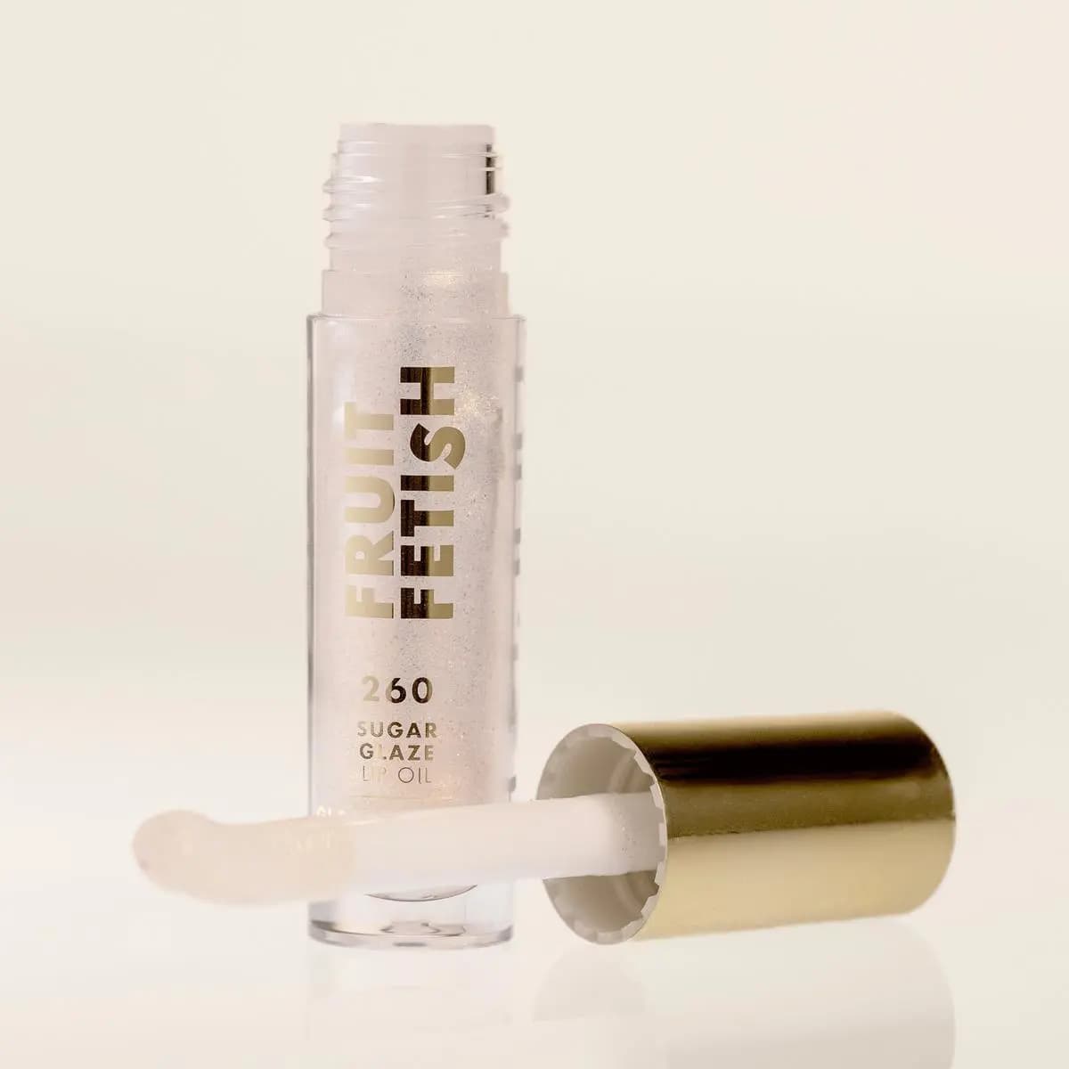 Sugar Glaze tube on a cream backdrop with its gold cap and shimmery clear applicator resting in front