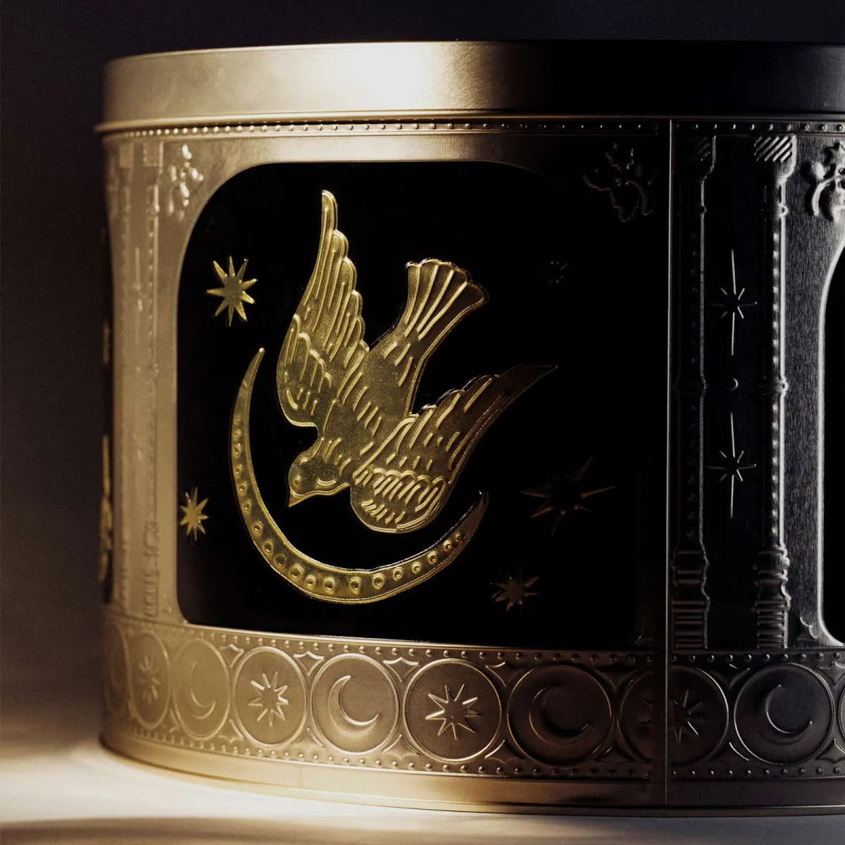 Dramatically lit tin panel showing a gold embossed swallow over a crescent moon among stars