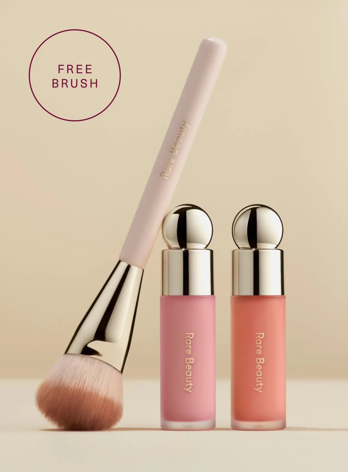 Pink-handled Rare Beauty blush brush leaning on pink and peach liquid blush bottles with gold caps, beside a Free Brush badge