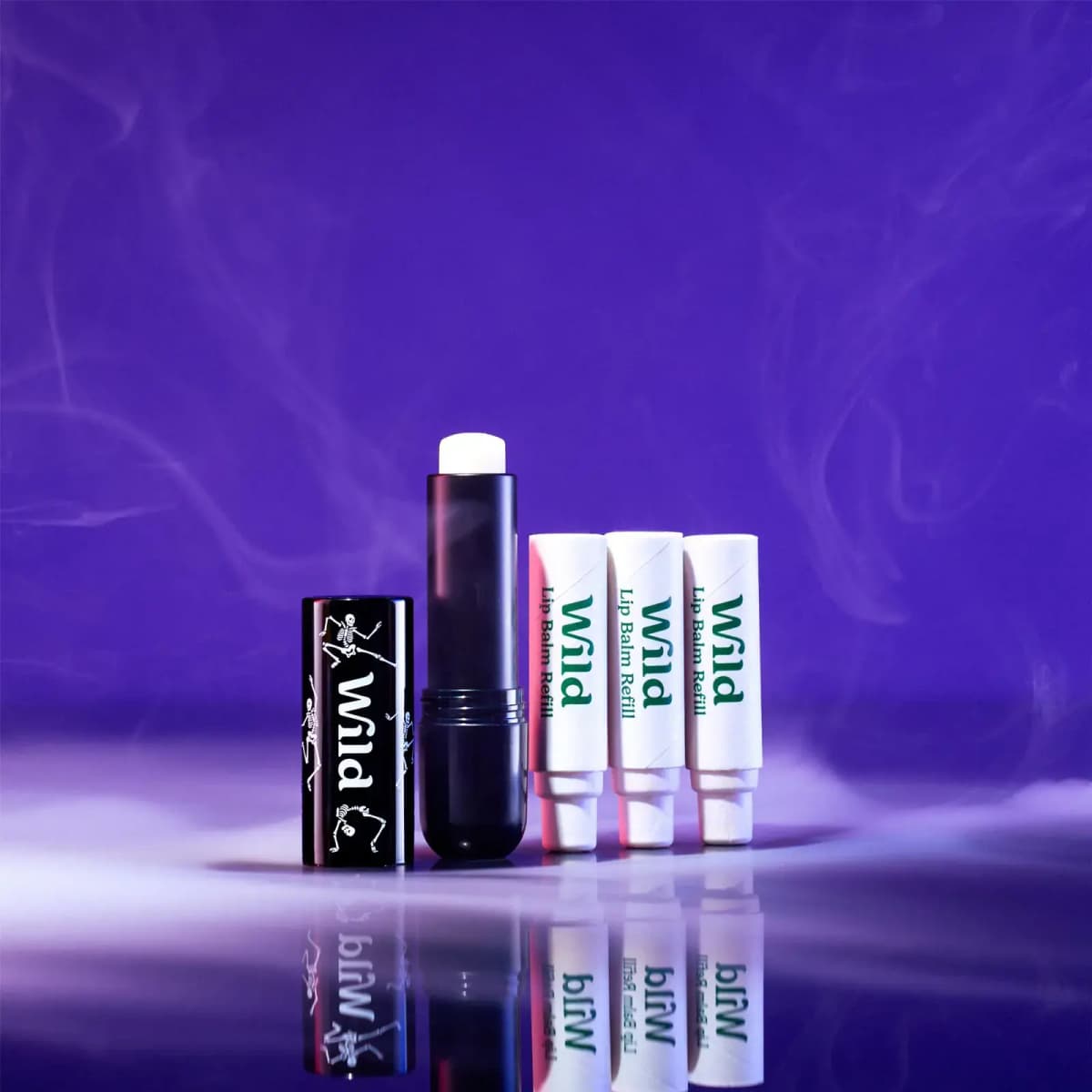 Black skeleton-print Wild lip balm case with three white Wild Lip Balm Refill tubes against a smoky violet background