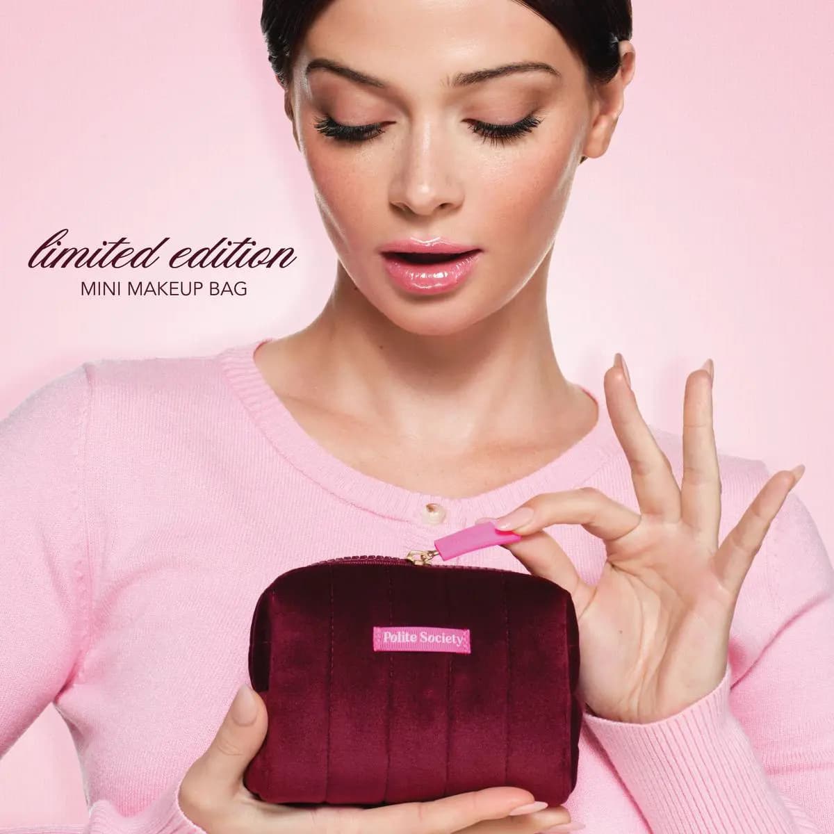 Model in pink cardigan holding the limited edition burgundy quilted mini makeup bag by its pink zipper pull
