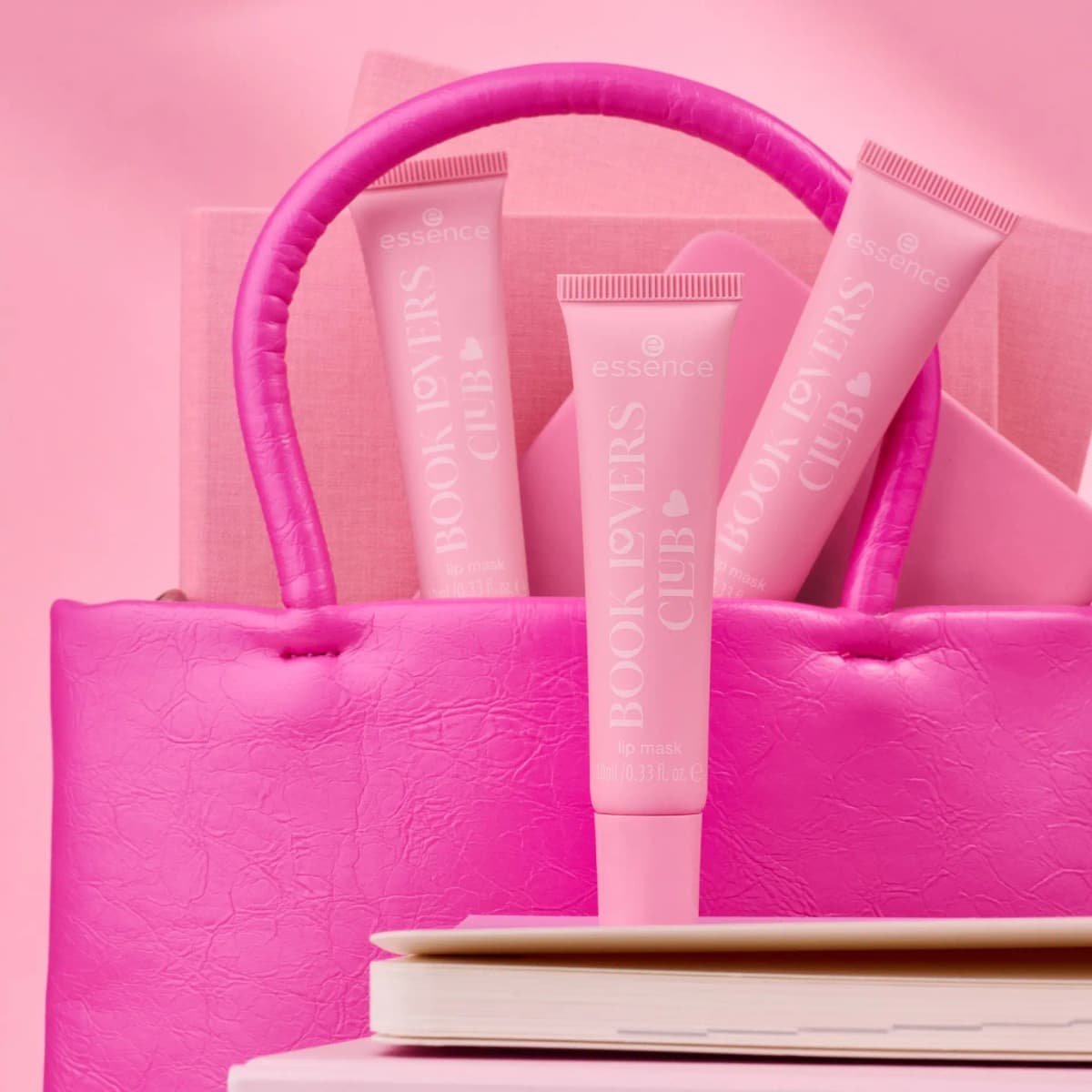 Three pink lip mask tubes standing in a hot pink leather handbag against a pink background