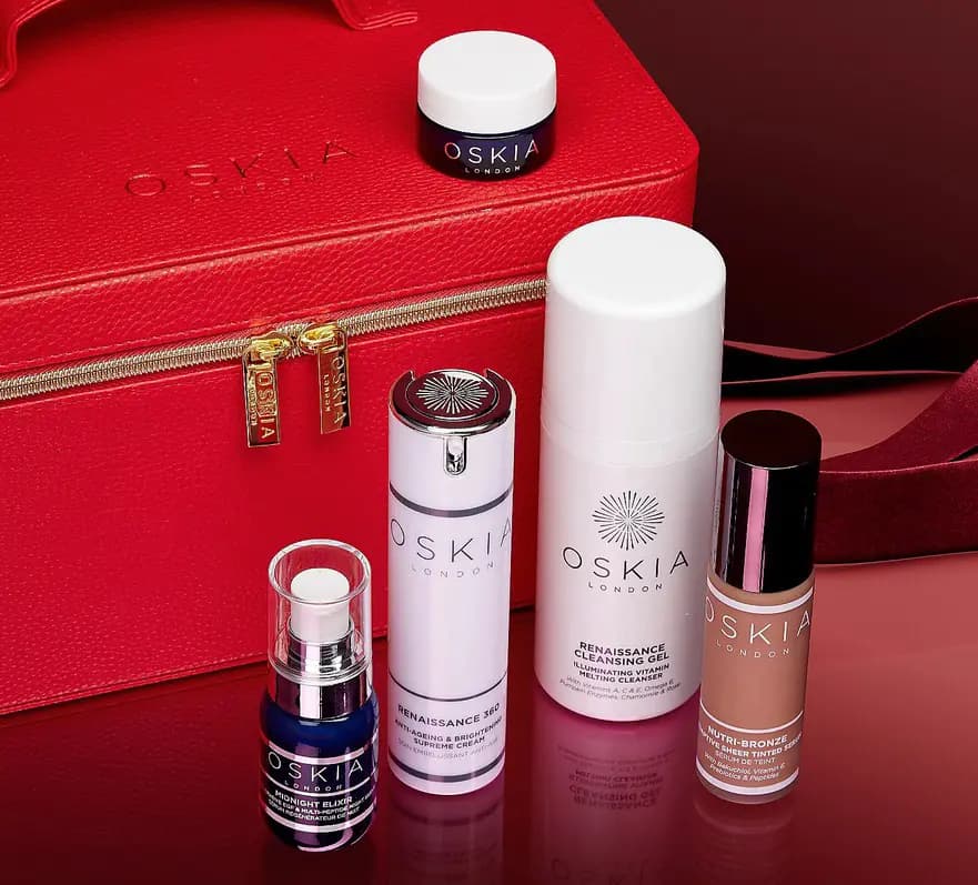 Red OSKIA vanity case with gold zip pulls and five OSKIA skincare products including Renaissance cream, cleansing gel