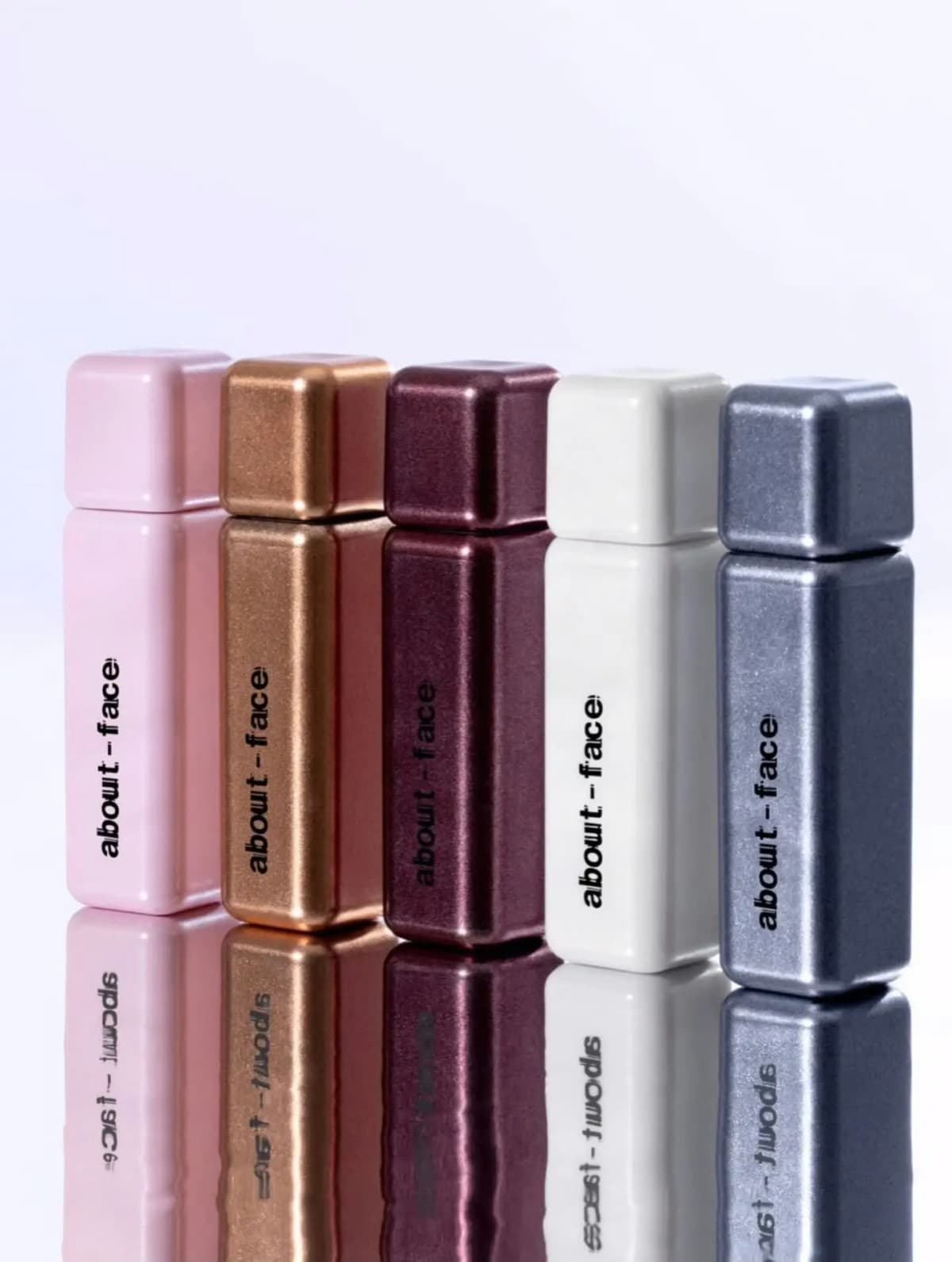 Five about-face square tubes in pink, bronze, plum, white and slate metallic finishes, reflected on a glossy surface