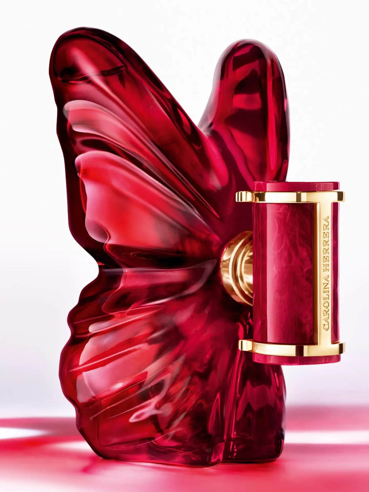 Berry-red Carolina Herrera La Bomba Intensa butterfly bottle with gold-framed marbled cap on a glowing pink surface