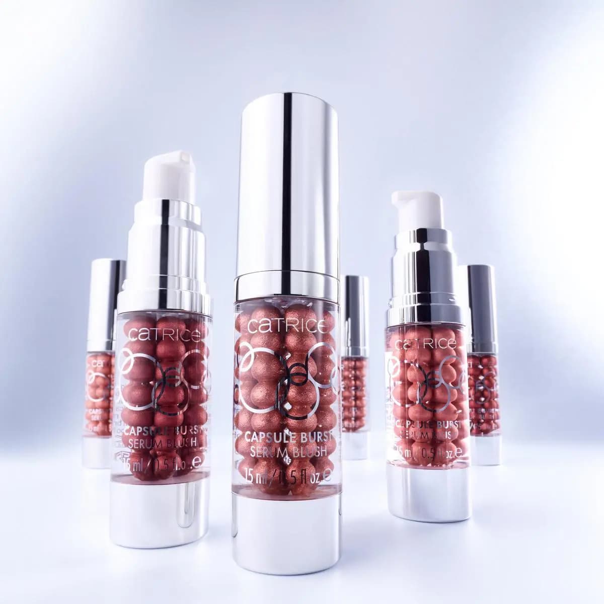 Several Capsule Burst Serum Blush pump bottles filled with copper-red shimmer beads