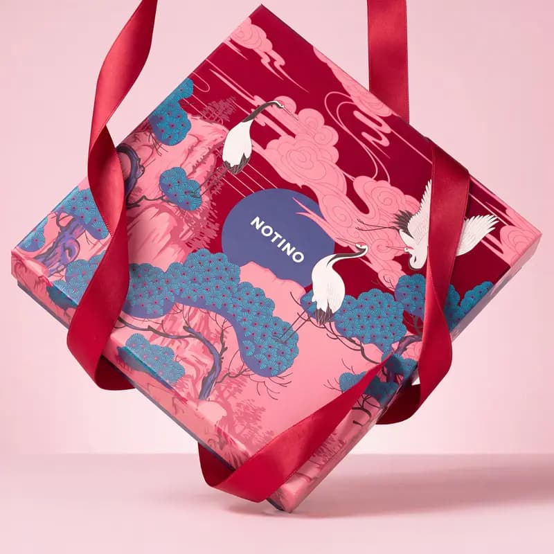 Pink and red Notino Korean Beauty Gems box featuring cranes and pine trees, tied with red ribbon handles