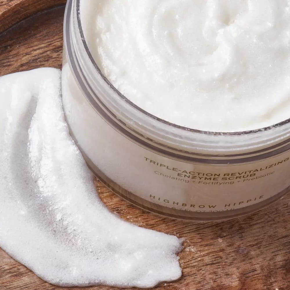 Close-up of white, sugary scrub texture swirled in the open jar beside a foamy white swatch on wood