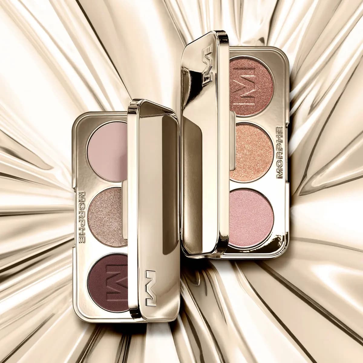 Two gold Morphe eyeshadow trios standing open on gold foil, one rosy and shimmery, one pink, taupe and plum