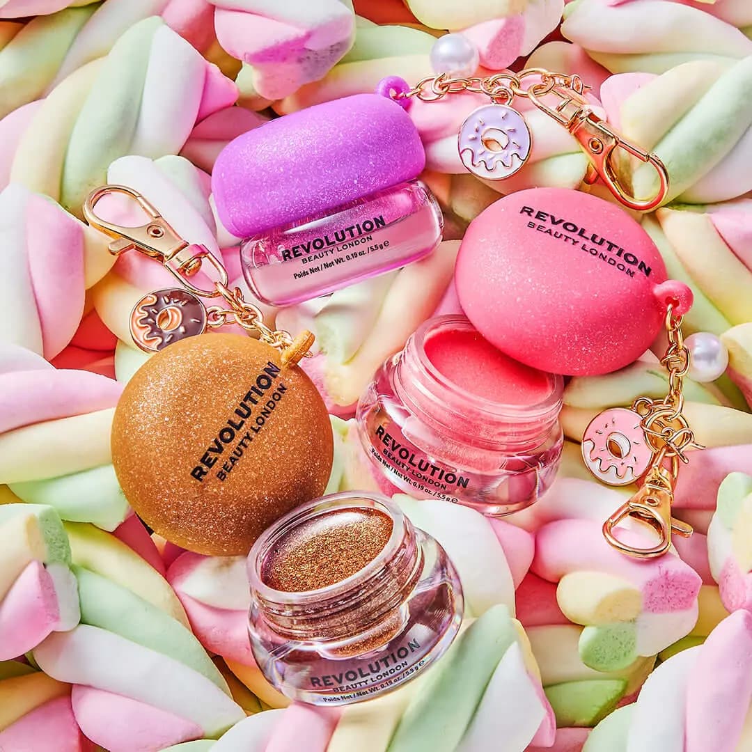 Pink, gold and lilac glitter-lidded jellies with open jars and donut charms on a bed of pastel marshmallows
