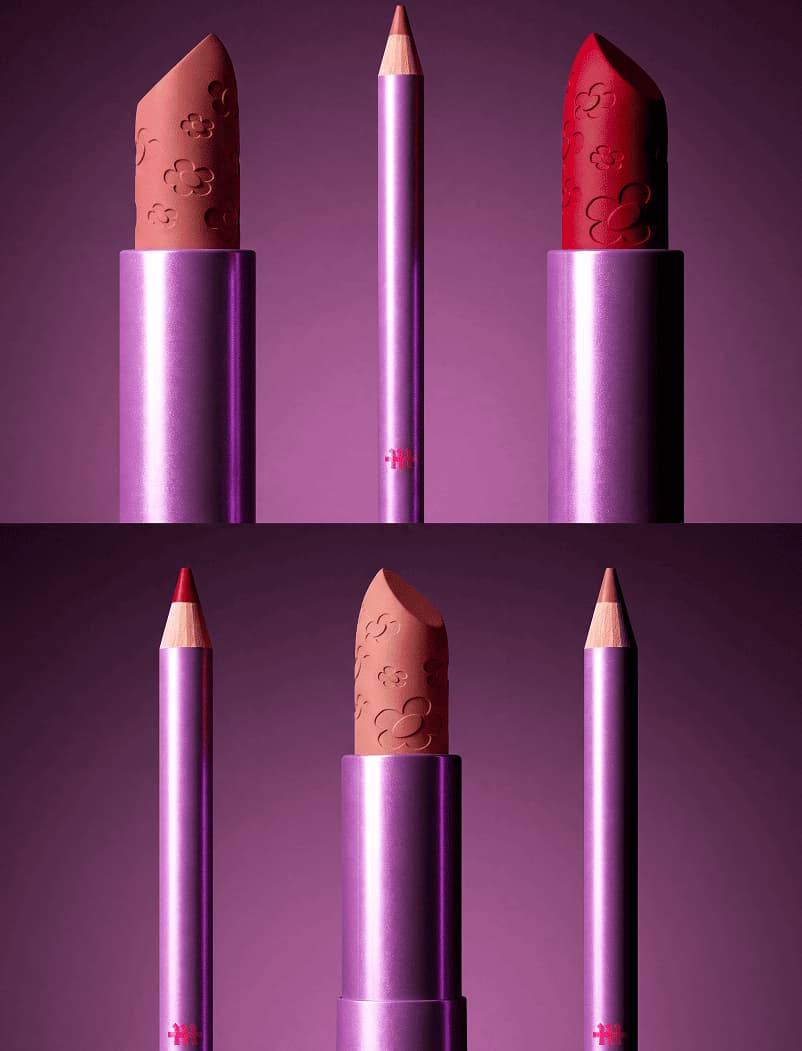 Close-up of two floral-embossed lipsticks in nude and red beside a lip liner pencil against purple lighting.