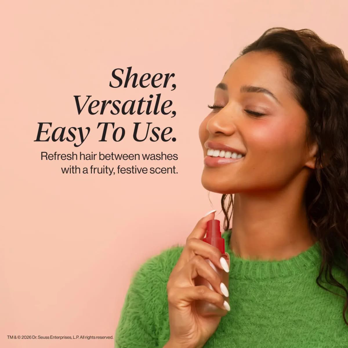 Smiling woman with dark curly hair in a green fuzzy sweater holds the red-capped mist near her chin, eyes closed