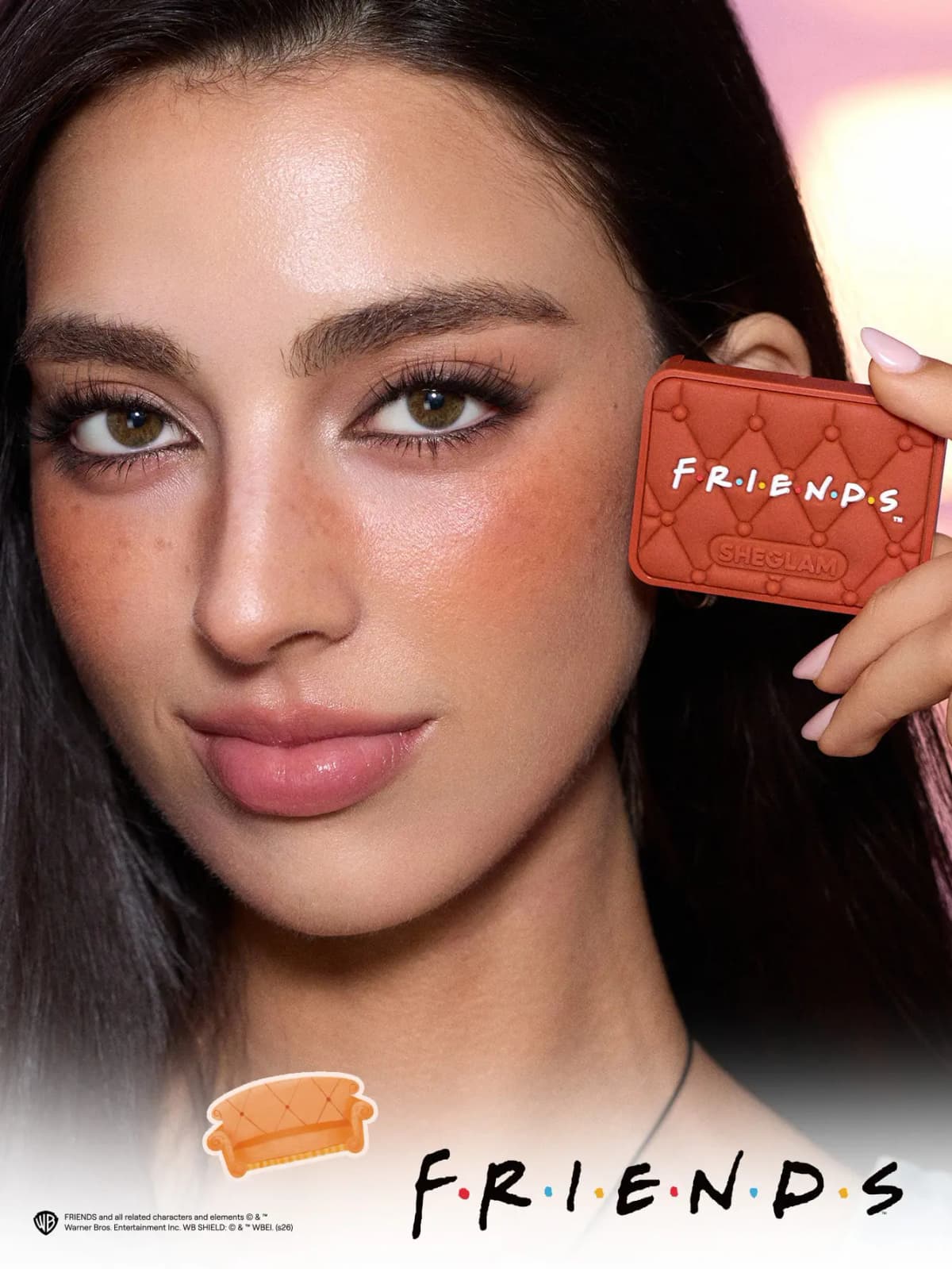 Dark-haired model with warm peachy flushed cheeks holds the tufted orange FRIENDS blush compact by her face