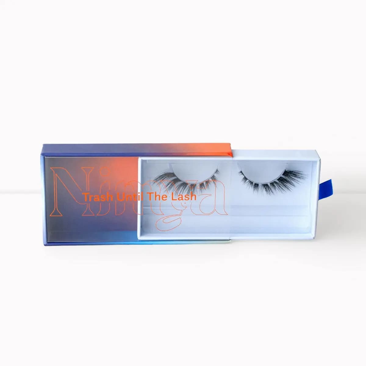 A single Nimya lash box slightly open showing a wispy natural strip lash inside, with blue ribbon pull tab.