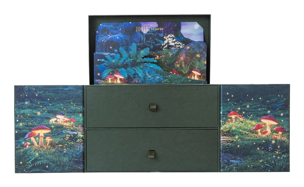 Closed two-drawer green chest with ribbon pulls, mushroom-printed side flaps and a pop-up forest card in the lid