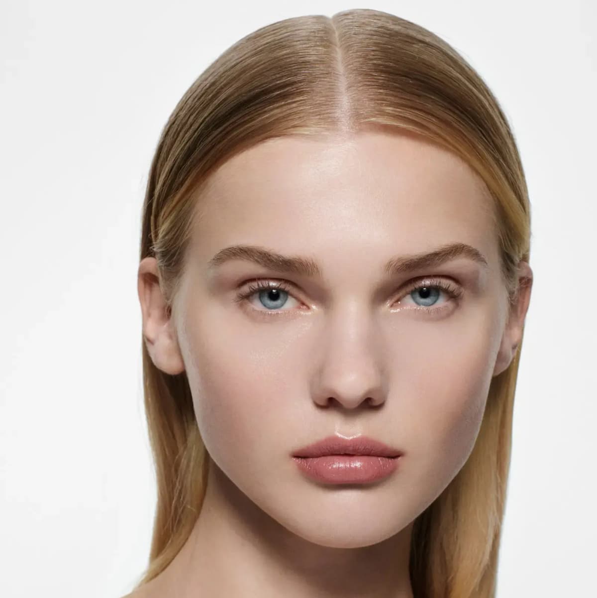 Blonde model with slicked-back centre-parted hair wearing a glossy rosy-nude lipstick
