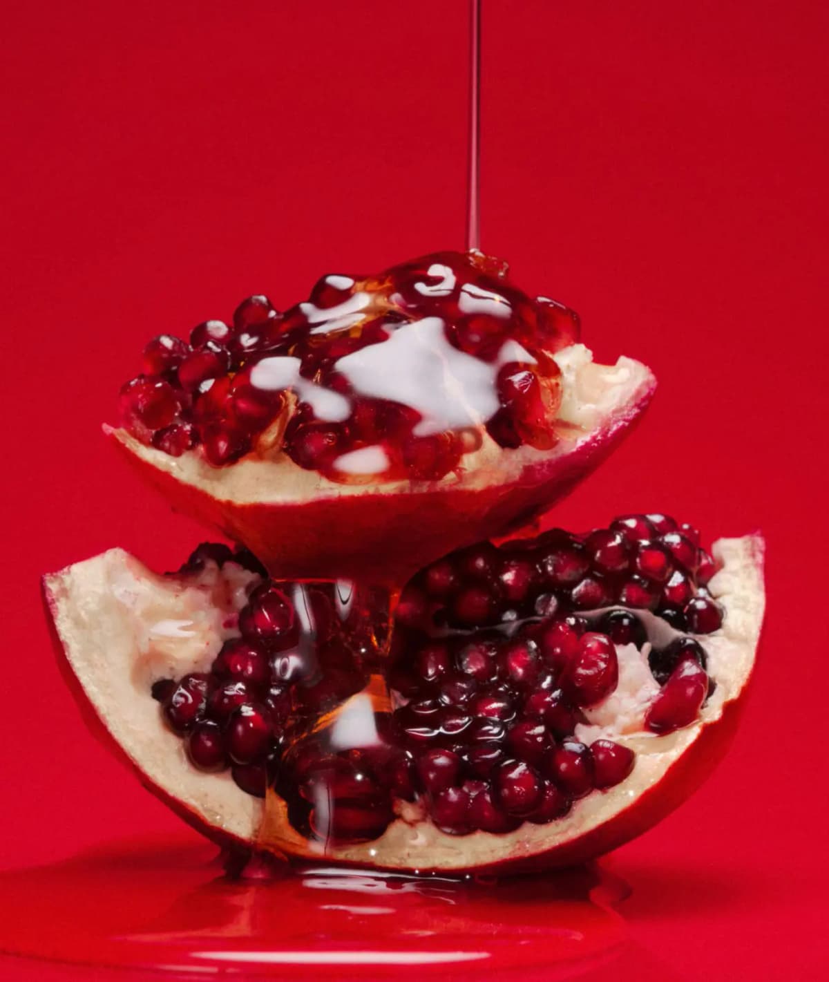 Stacked pomegranate halves glistening with a pour of honey-like syrup and white cream on red